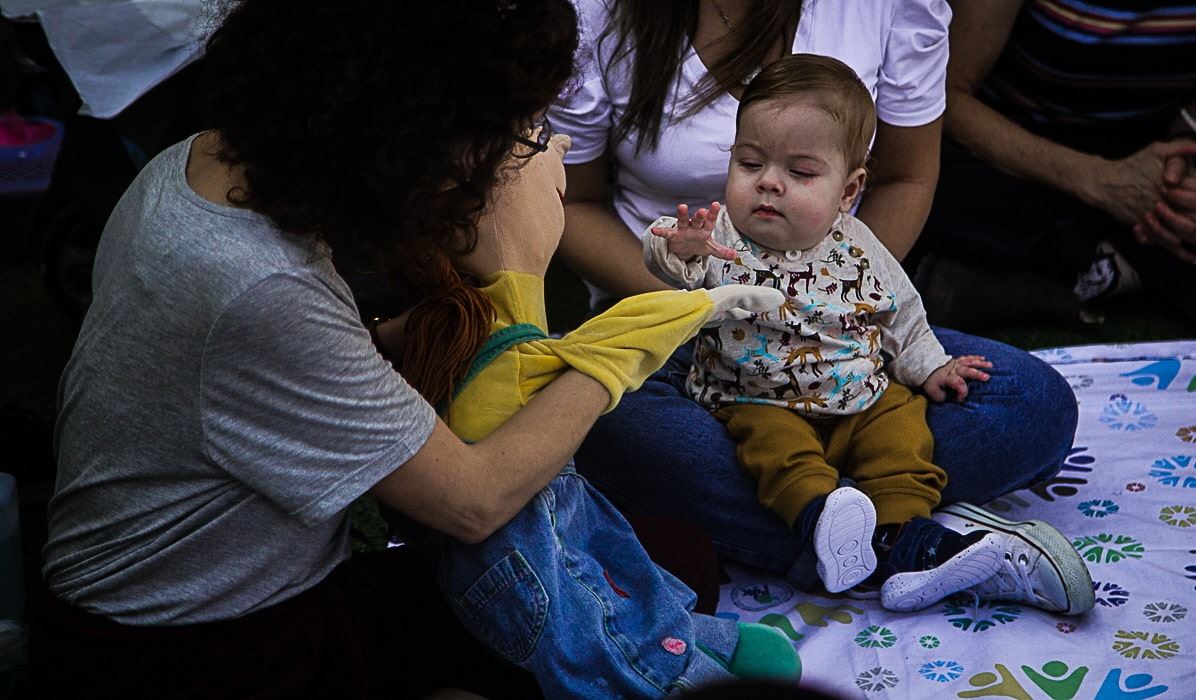 תינוק יושב על שמיכה פרחונית, ומטפלת מקצועית בבית חולים אלי